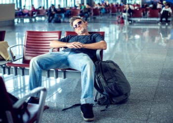 Man with sunglasses sleeping while sitting in airport terminal and waiting for flight departure