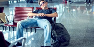 Man with sunglasses sleeping while sitting in airport terminal and waiting for flight departure